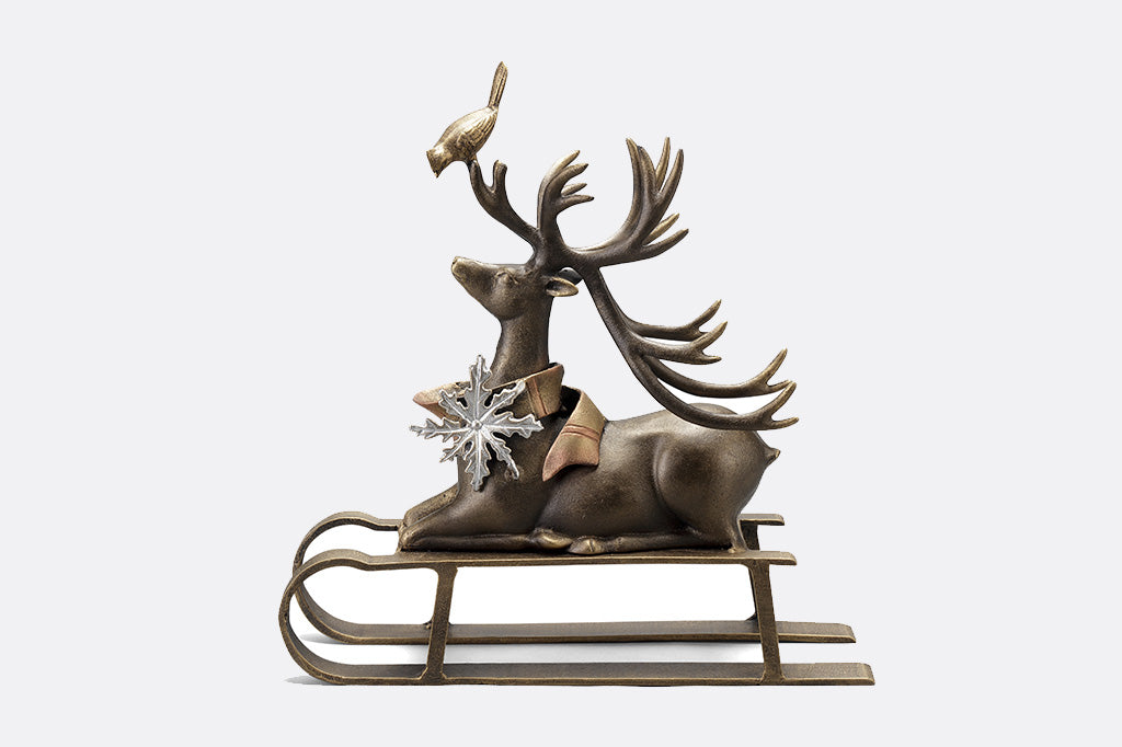 Cast aluminum reindeer sculpture with little bird friend on antlers seated on a sled left side profile 