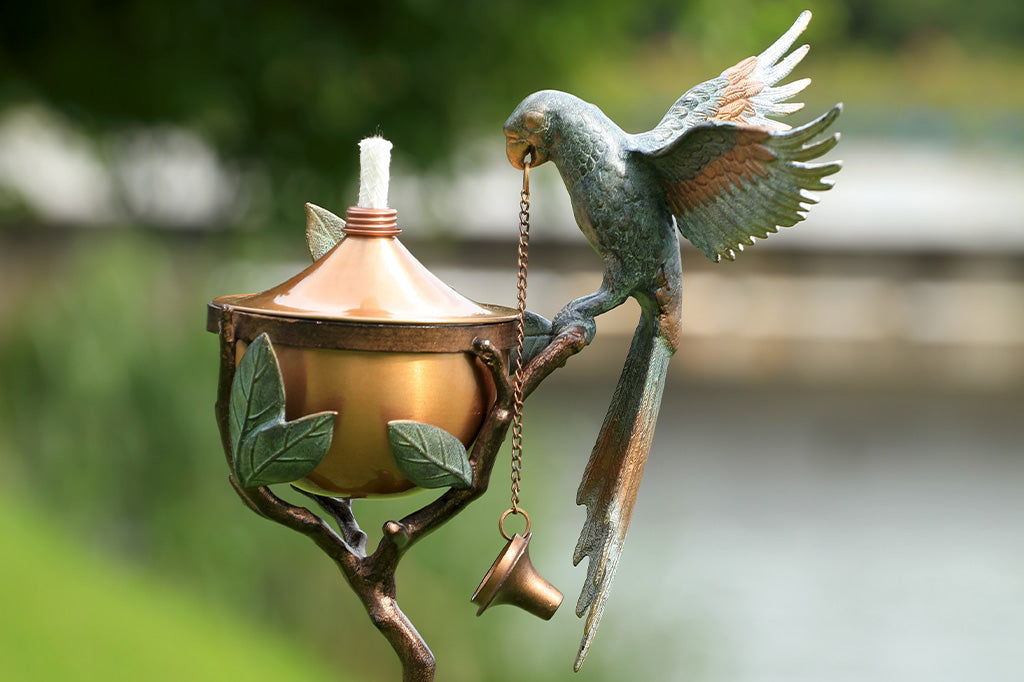 Outdoor Garden Torch with parrot on a leafy branch. Wings outstretched. Torch shown in garden.
