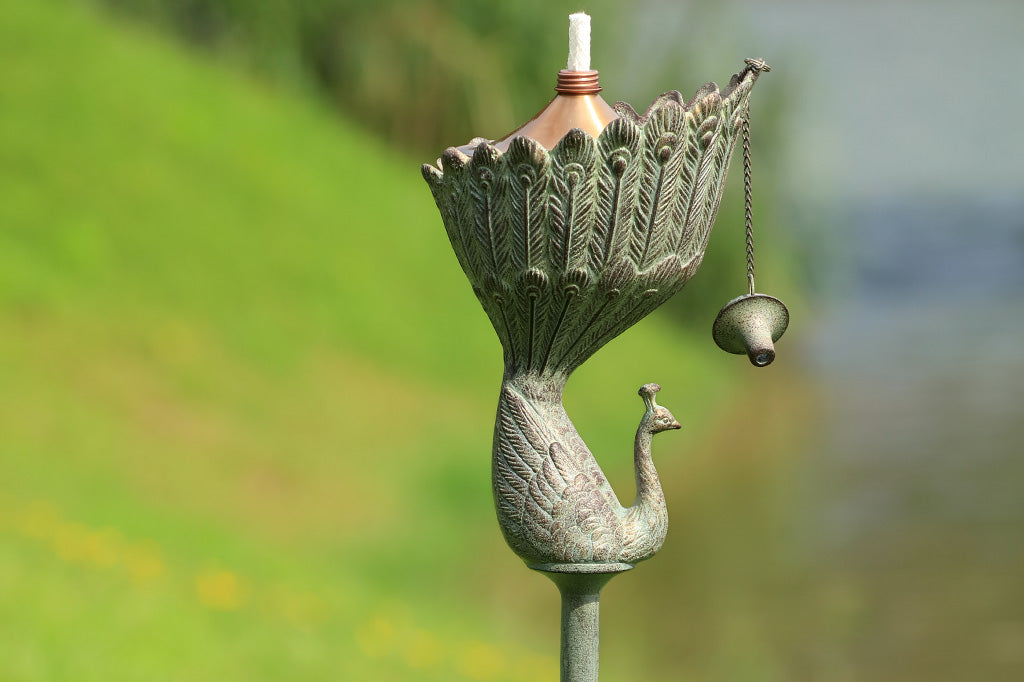Peacock shaped garden oil torch in verdigris finish shown in yard
