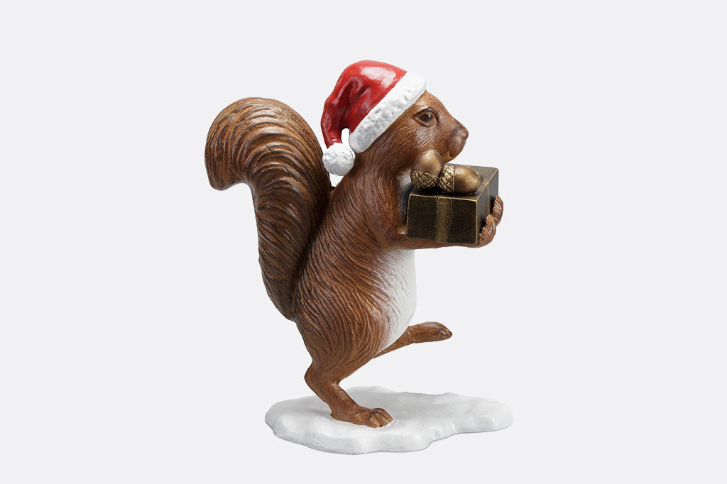 Brown squirrel sculpture on his way to delver presents and acorns wearing a red santa hat