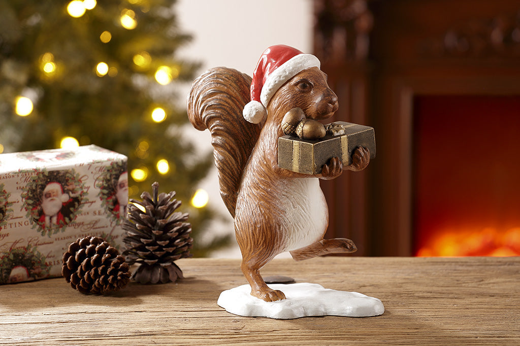 Brown squirrel sculpture on his way to delver presents and acorns wearing a red santa hat  