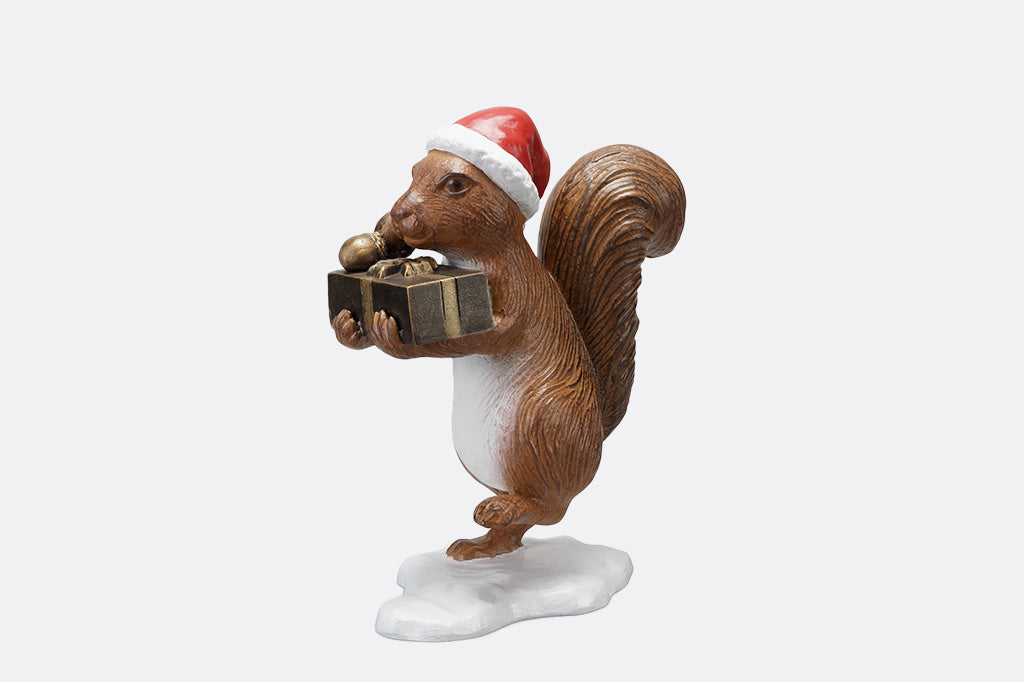 Brown squirrel sculpture on his way to delver presents and acorns wearing a red santa hat