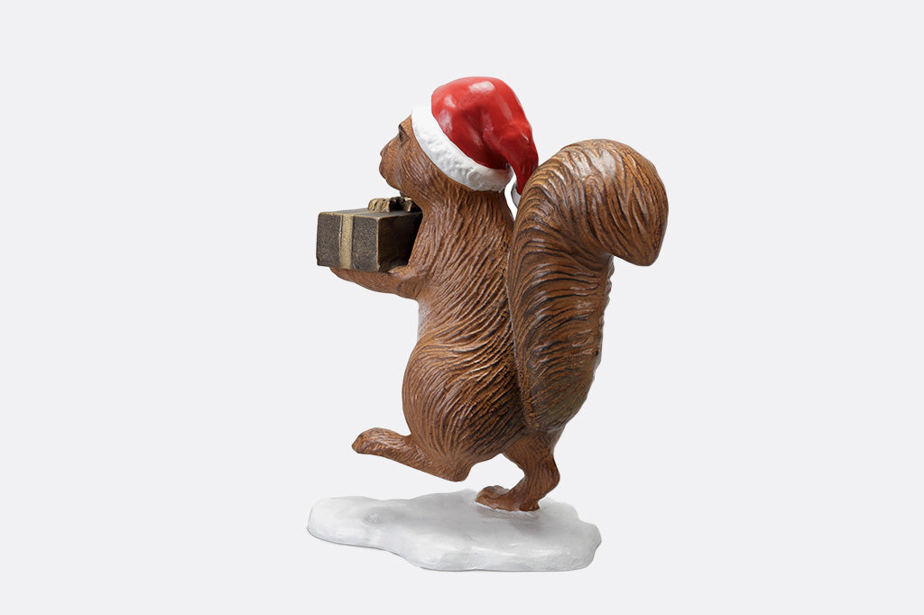 Brown squirrel sculpture on his way to delver presents and acorns wearing a red santa with a fluffy tail hat back view 