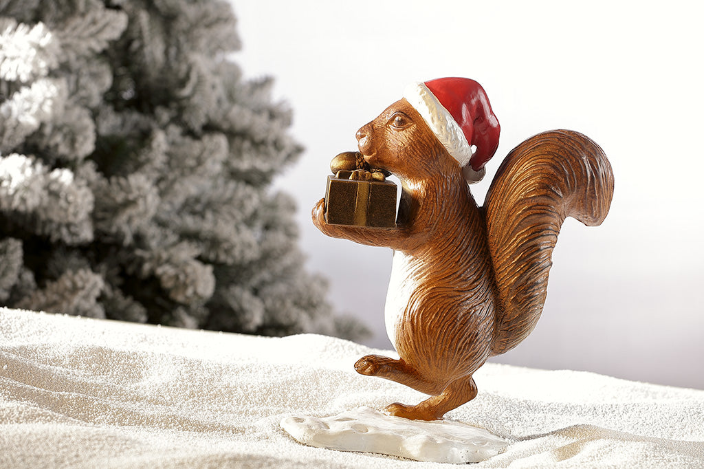 Brown squirrel sculpture on his way to delver presents and acorns wearing a red santa hat