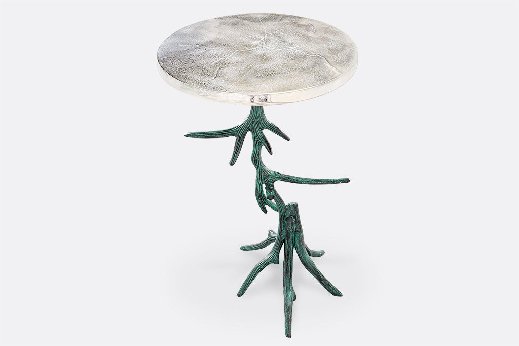 Lodge style table shows sculpted antlers in verdigris finish as the base of a textured silver table top