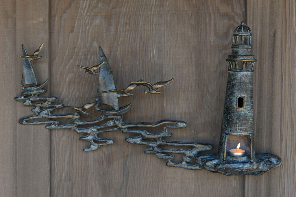 Wall art Votive holder cast metal sculpture of Lighthouse by the sea with 2 sail boats on a wood wall