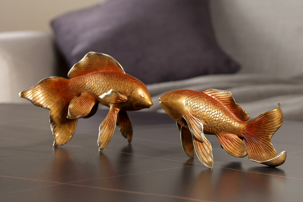 Two golden orange koi fish sculptures on a coffee table by a couch with purple pillow