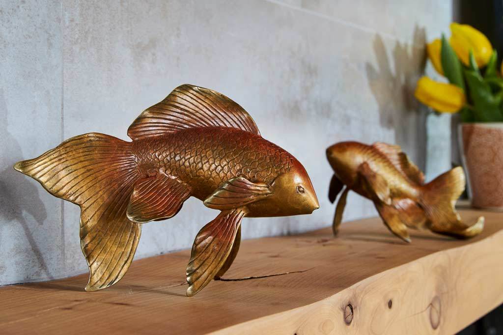Two golden orange koi fish sculptures on a fireplace mantle next to tulips