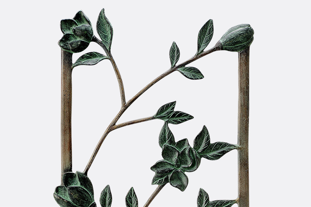 Magnolias Trellis Tall is cast metal with verdigris blossoms and branches on a bronze frame, close up view