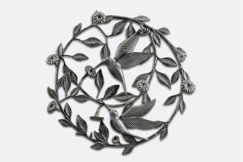 Large circular wall art made from cast metal in a motif of flowering vines and 2 sipping hummingbirds
