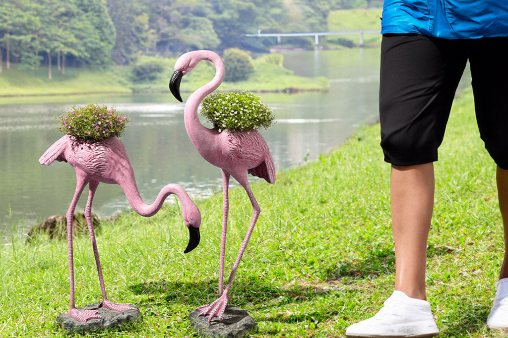 person walking by the outdoor flamingo planters on a lawn