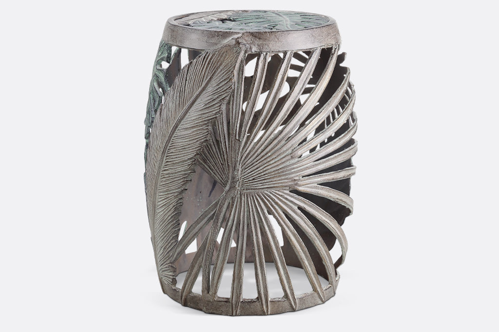 Las Palmas Garden Stool is adorned on all sides with a variety of hand sculpted tropical leaves. The leaves on this stool have been finished in verdigris and bronze over cast aluminum. Banana leaf, fan palm, and monstera leaf motifs surround the stool.