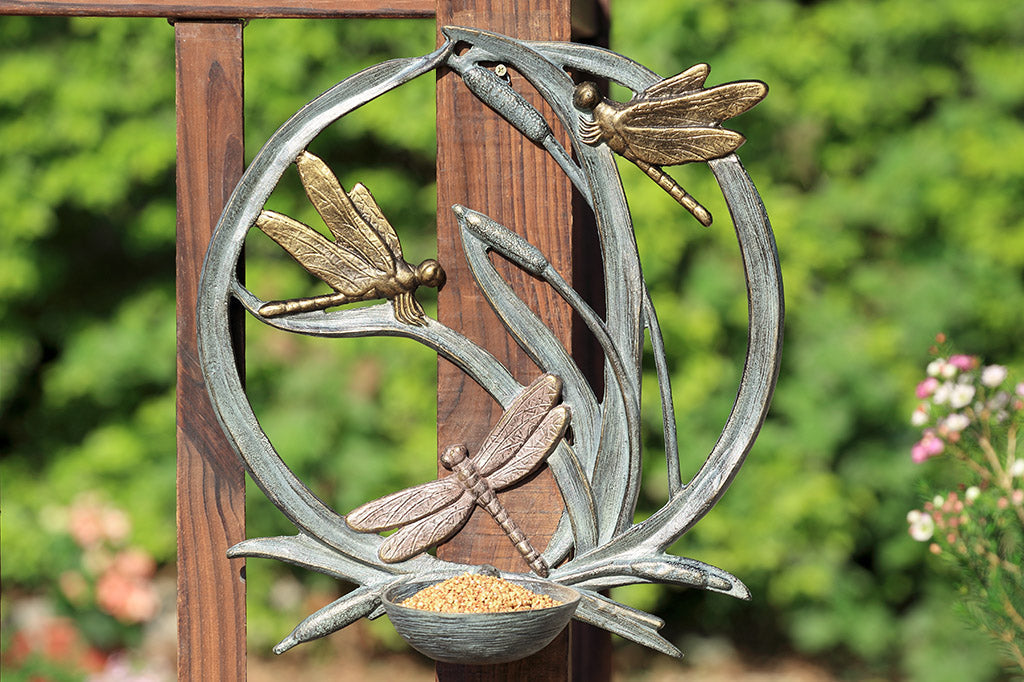 birdfeeder station that hangs on walls with dragonfly and cattail motif shown hung on fence rail