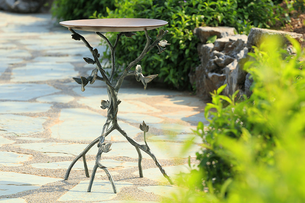 Hummingbird and Flowers Birdbath with sculpted metal birds and blossoms, on a patio in a garden