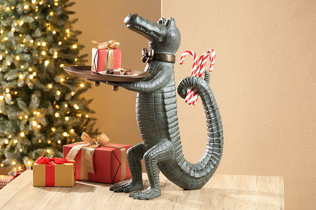 Holiday décor: Standing Crocodile dressed as a butler holds a serving tray whilst hiding candy canes behind its back. Shown on table in a Christmas living room scene with wrapped gifts.