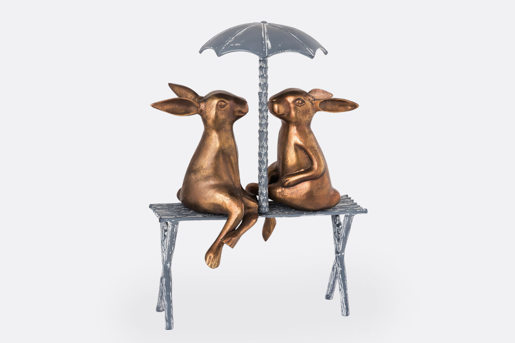 Two Rabbits sit on a bench under an umbrella
