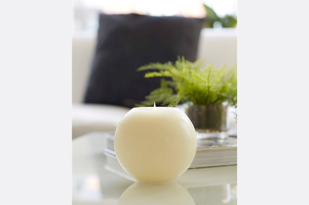round LED candle in ivory shown on coffee table near books and fern